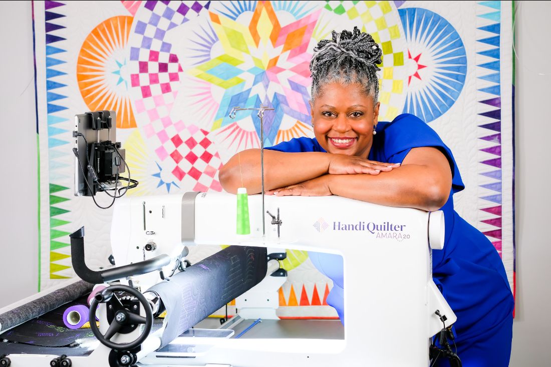Tina Harris leaning on a longarm machine with a beautiful quilt in the background